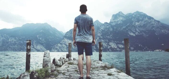 Man Standing Near the Ocean and Mountains